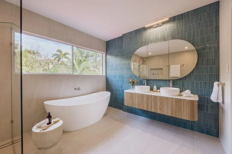 Bathroom with a freestanding bath, oval mirror, timber vanity and teal tiled wall