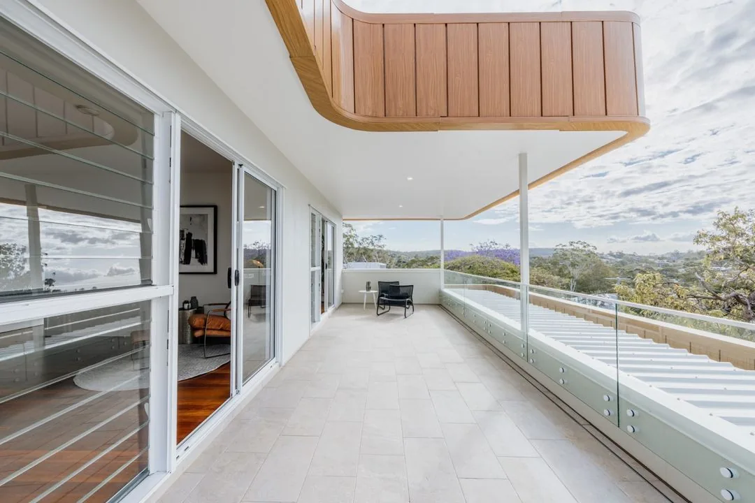 Covered deck running along the upper level, with glass balustrade, timber soffit and views across the valley