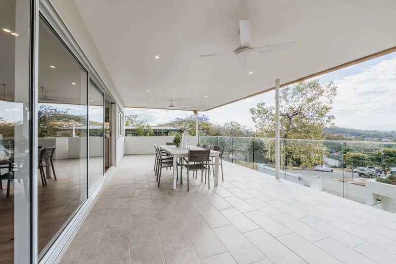 Sliding glass doors opening the living area onto a covered terrace with glass balustrade and a district outlook