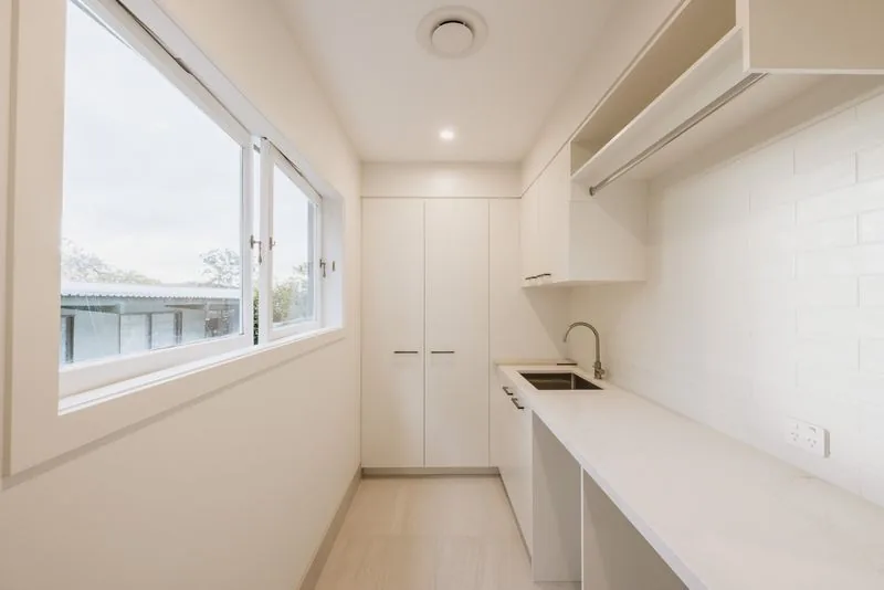 Galley laundry with white cabinetry, a full-length benchtop and a window to the garden