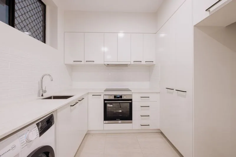 Utility kitchenette with white cabinetry, integrated appliances and a laundry bay