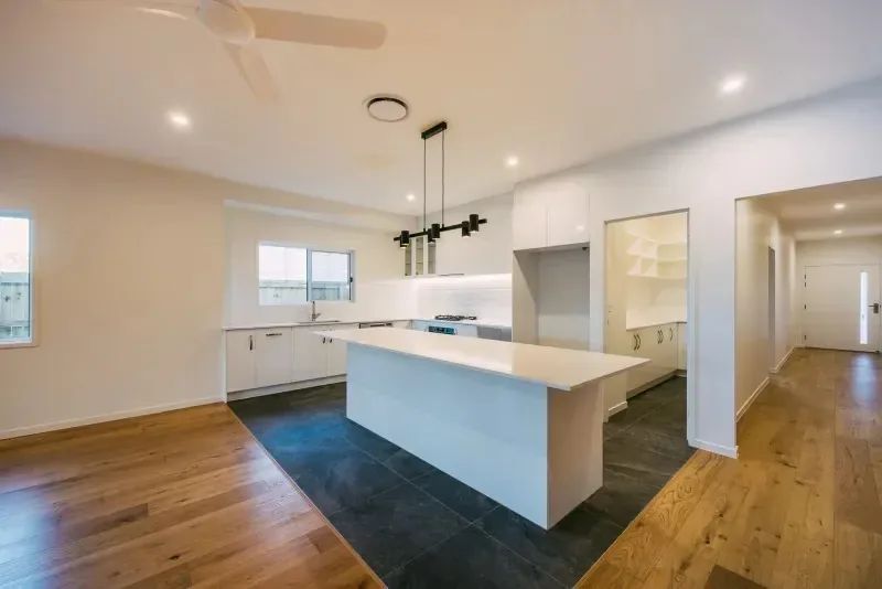Kitchen with a stone island bench, pendant lighting and a tiled floor zone against engineered timber