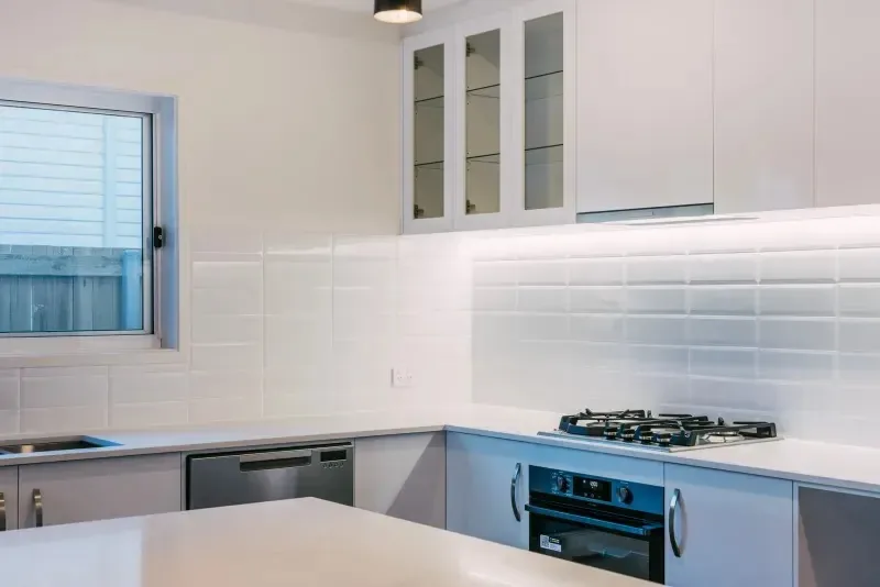Kitchen detail with a white tiled splashback, gas cooktop, wall oven and glazed overhead cabinets