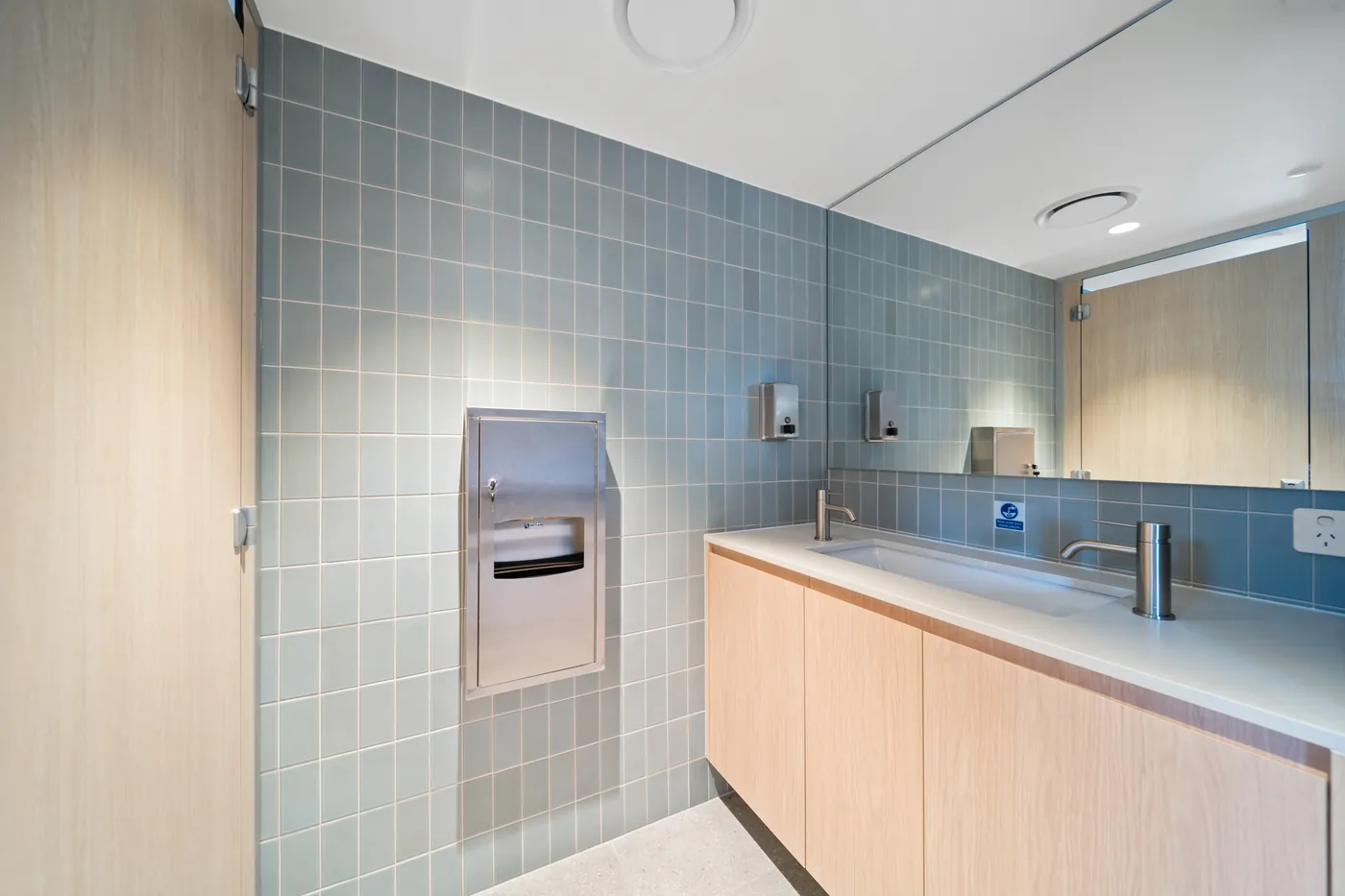 Staff amenities at the Sumner fit-out with pale blue tiling, a timber vanity and a full-width mirror