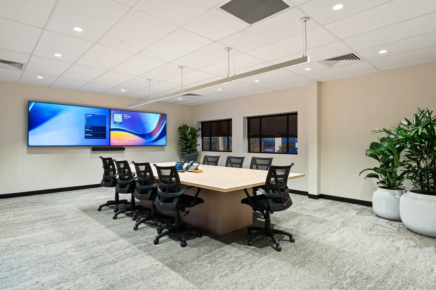 Boardroom with a long timber table, mesh task chairs and twin wall-mounted screens for conferencing