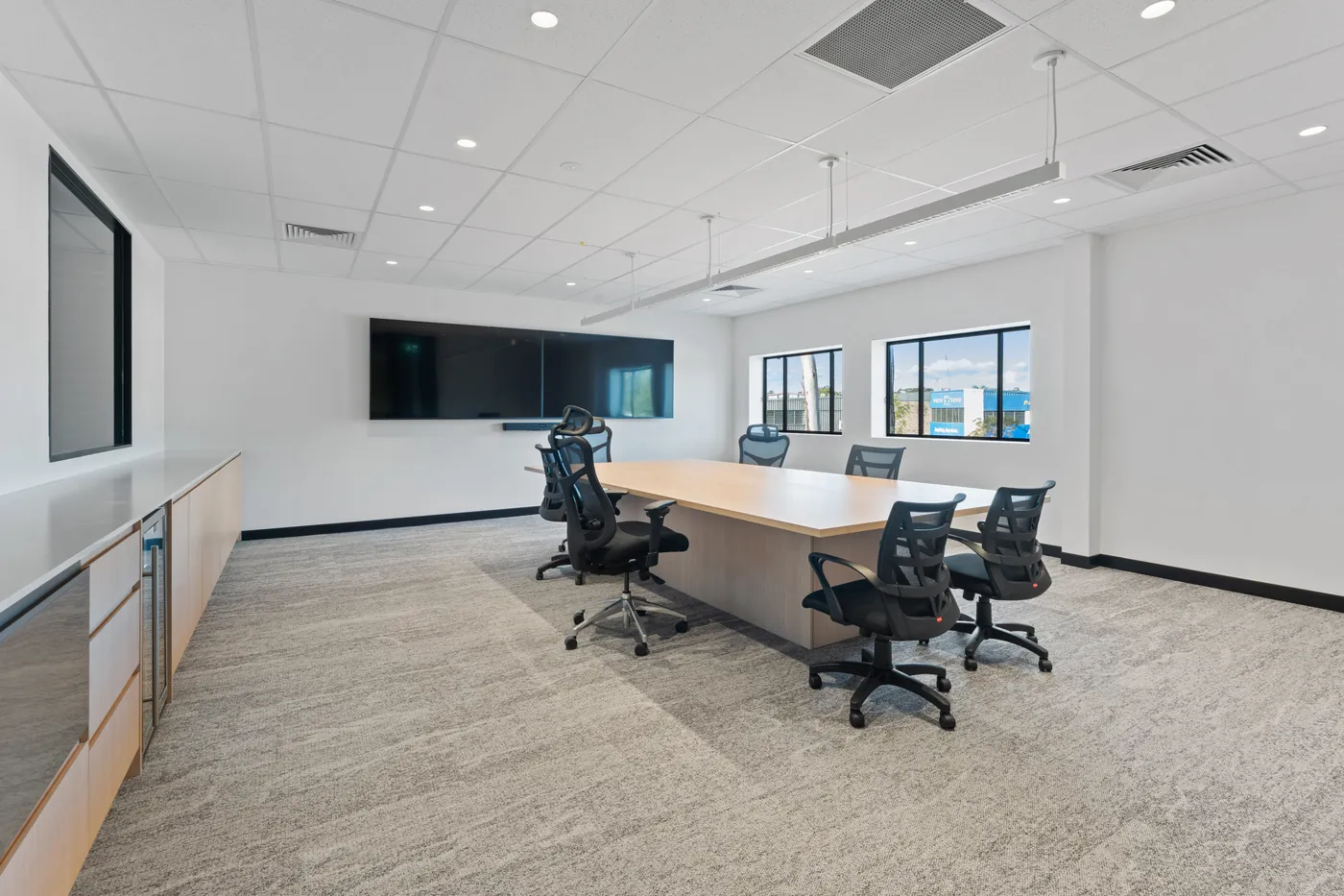 Boardroom at the Sumner fit-out with a long timber table, mesh task chairs, twin wall-mounted screens and suspended linear lighting