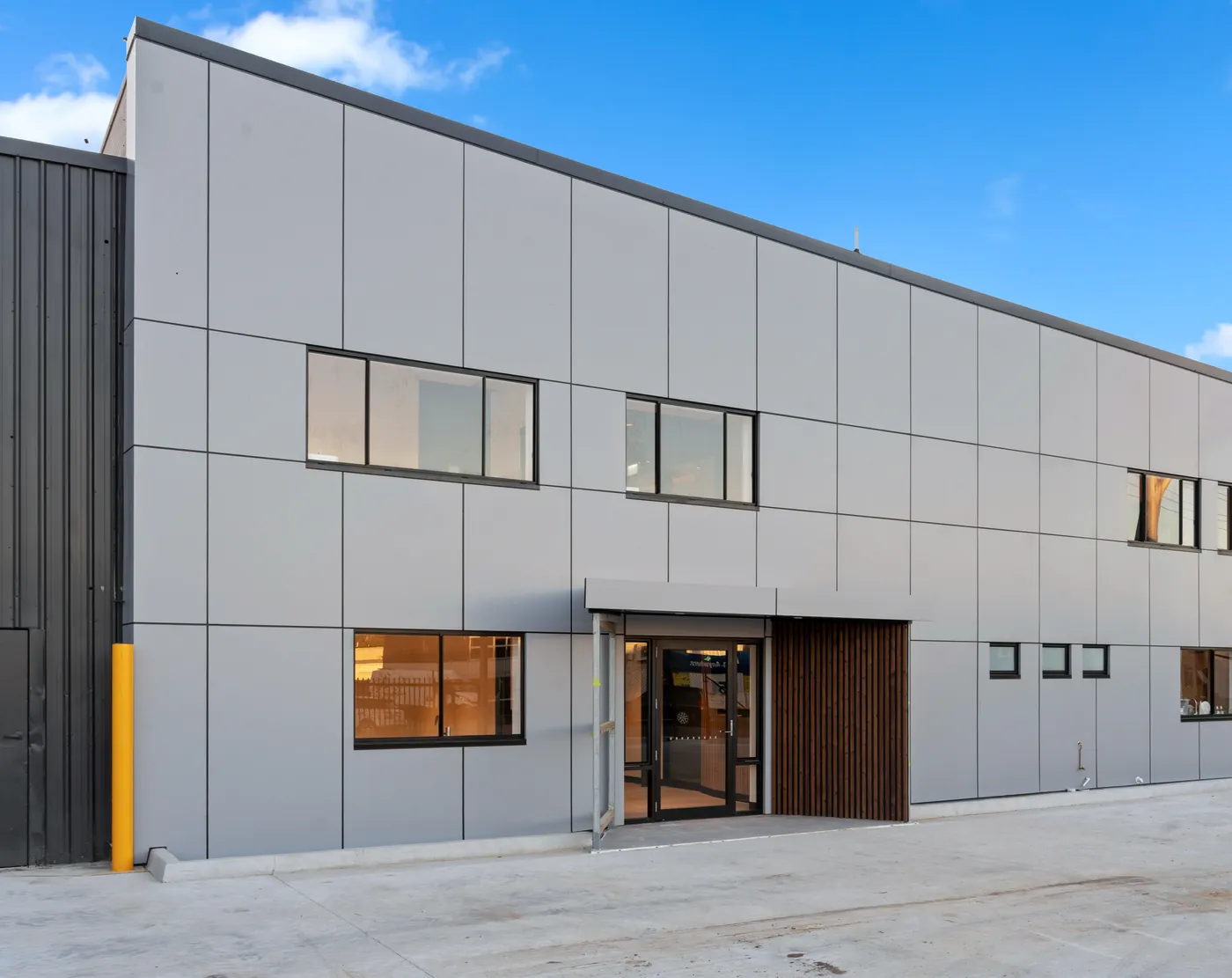 Two-storey commercial building at the Sumner fit-out, clad in grey composite panels with a timber batten entry