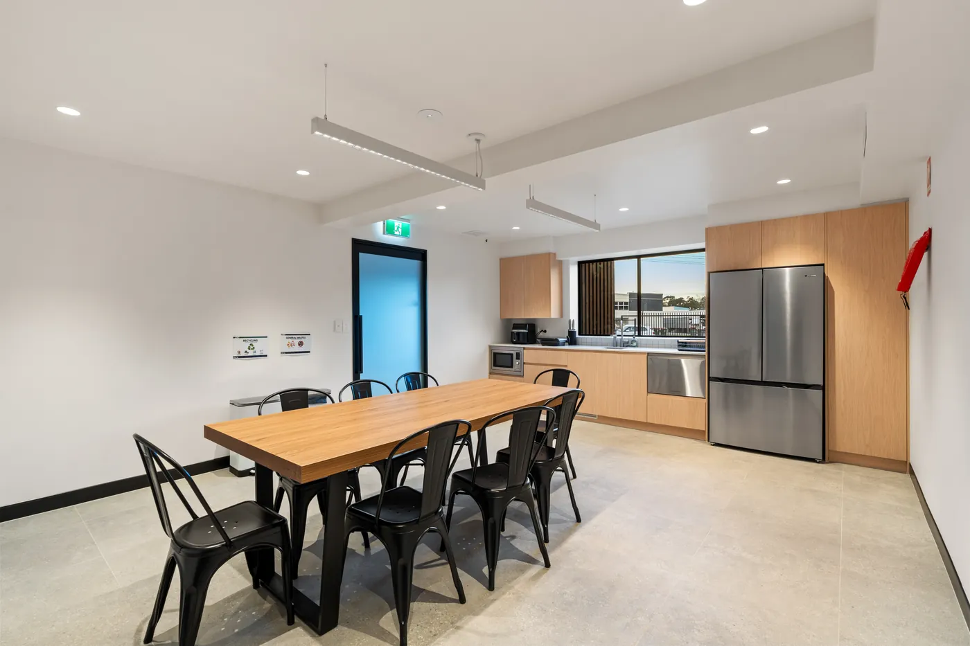 Staff lunch room with a timber table, black metal chairs and a full kitchen along the rear wall