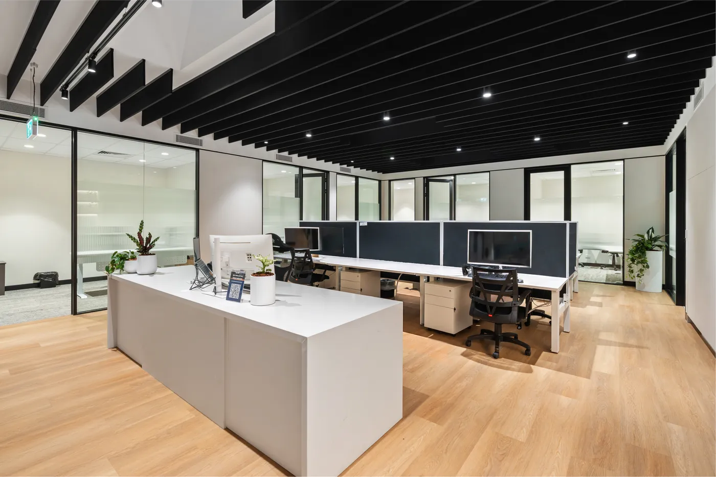 Open plan office with a reception bench, workstations behind acoustic screens and glazed meeting rooms beyond