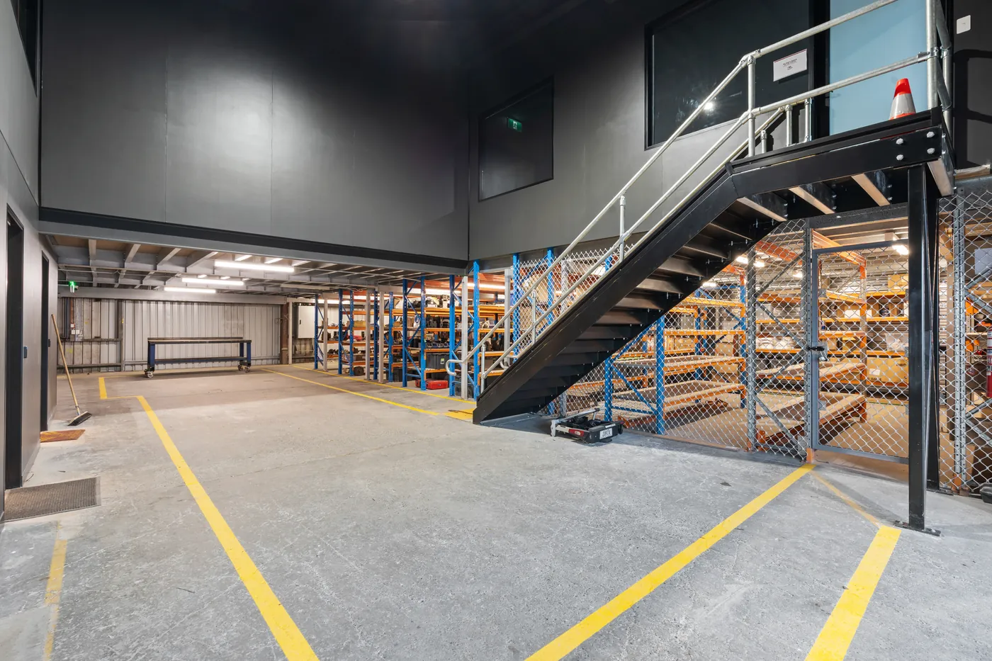 Steel stair rising to the mezzanine office above the warehouse, alongside secure caged storage