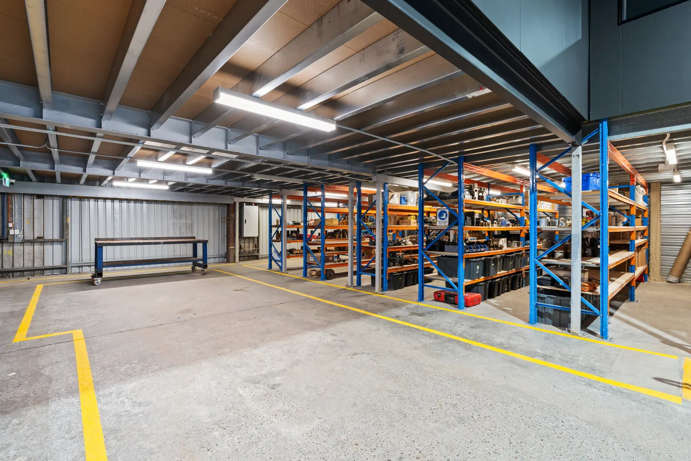 Warehouse floor beneath the new mezzanine, with racking, line-marked walkways and a steel-framed structure overhead