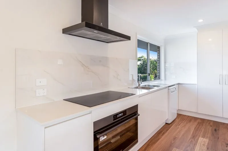 Kitchen with induction cooktop, integrated rangehood, stone splashback and white cabinetry