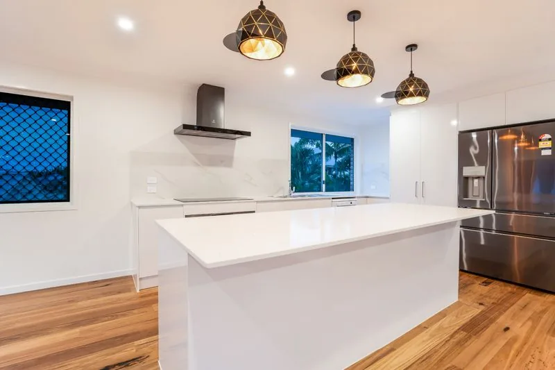 Kitchen with a stone island bench, pendant lighting, rangehood and hardwood floors