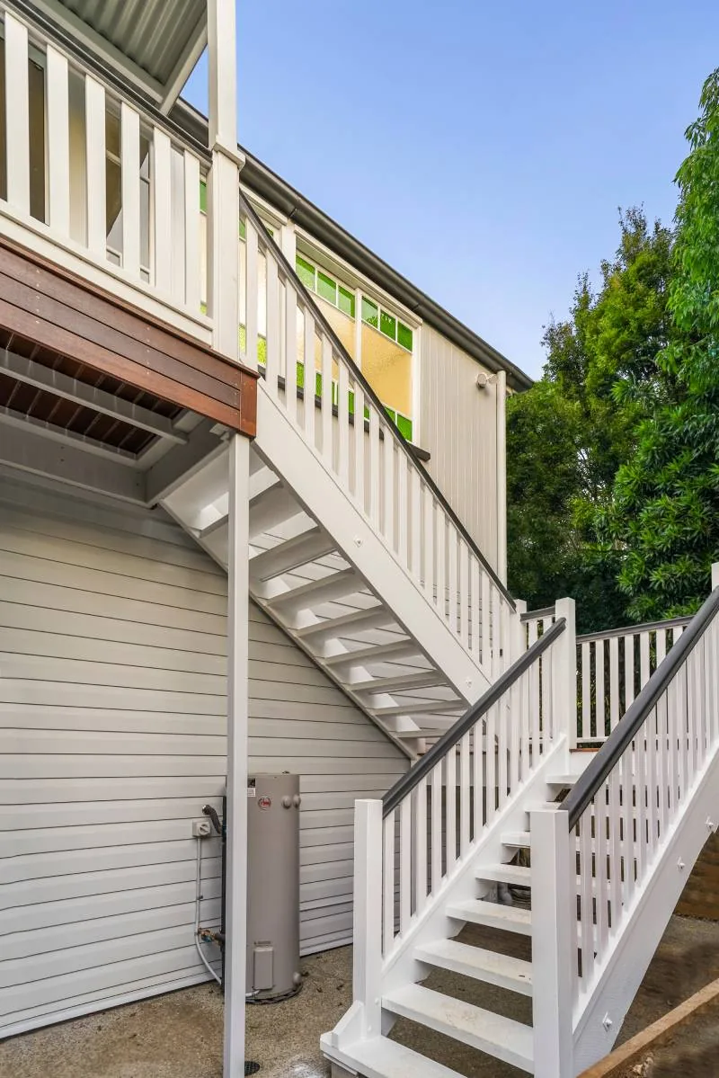 Rear exterior showing the painted timber stair, weatherboard cladding and the hot water unit