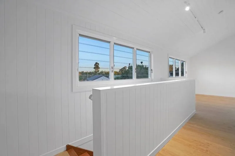 Upper level looking across the stair void, with VJ panelled walls, timber flooring and windows to the street