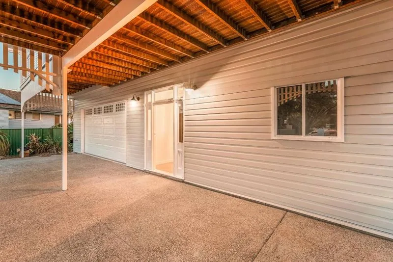Undercroft beneath the Queenslander, with exposed timber floor joists overhead, weatherboard walls and a poured concrete slab