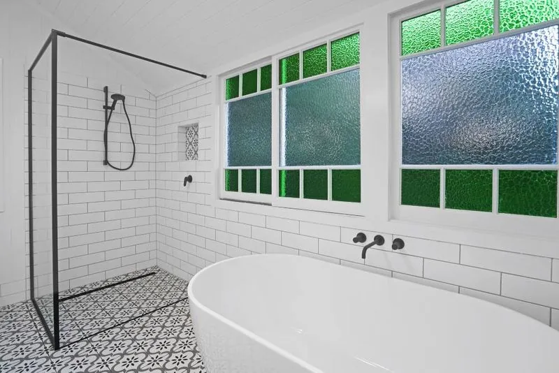 Freestanding bath set below leadlight windows, beside a walk-in shower with black fittings and patterned floor tiles