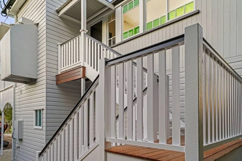 Exterior detail of the rear stair, with white balustrade and timber treads against weatherboard cladding and leadlight windows above