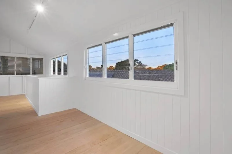 Open interior with VJ panelled walls, a raked ceiling, engineered timber flooring and windows facing the street