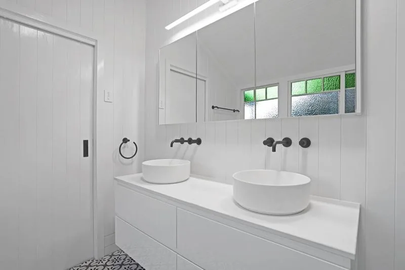 Bathroom vanity with twin vessel basins, black wall-mounted tapware, a full-width mirror and a leadlight window