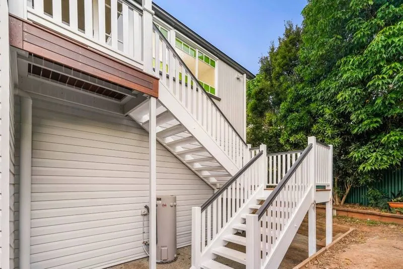 Timber and white painted stair rising to the rear deck, framed by weatherboard cladding and established trees
