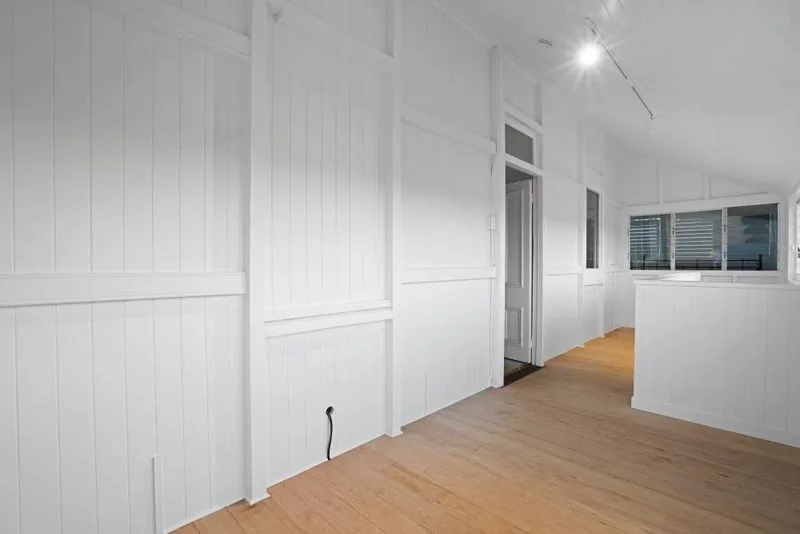 Empty interior room with VJ panelled walls, a raked ceiling and engineered timber flooring