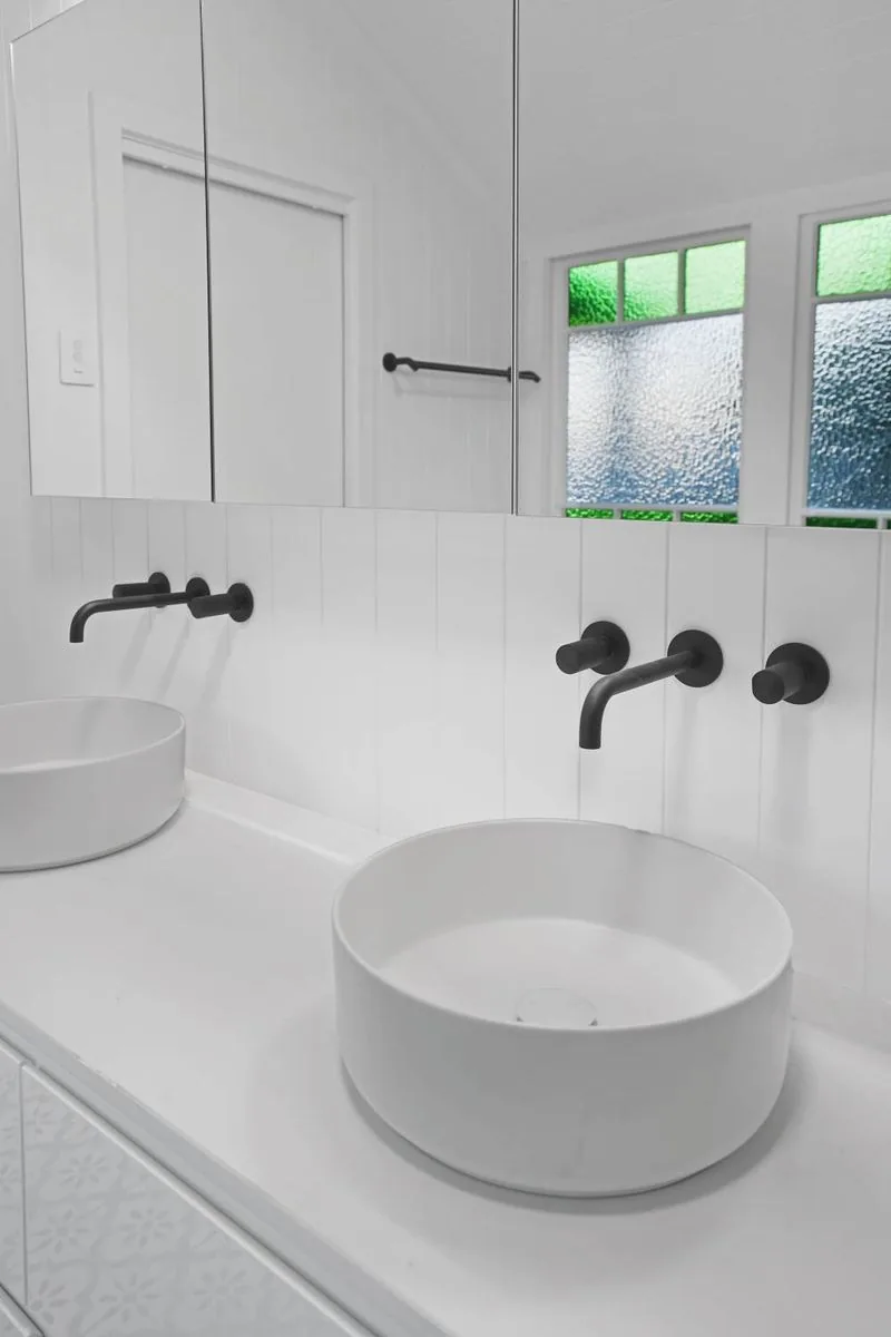 Close view of a vessel basin with black wall-mounted tapware against leadlight glazing