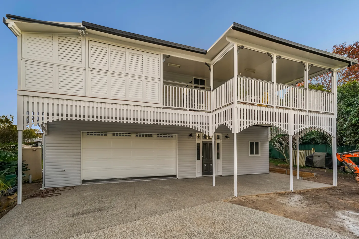 Wynnum West Queenslander after its exterior renovation, with white weatherboard, a full-width verandah and balustrade, and a double garage beneath